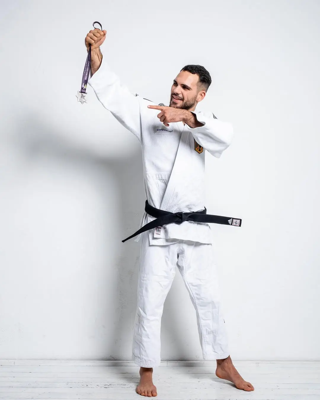 Lennart Sass zeigt Medaille Lennart Sass im weißen Judogi mit schwarzem Gürtel hält eine Medaille hoch und zeigt darauf